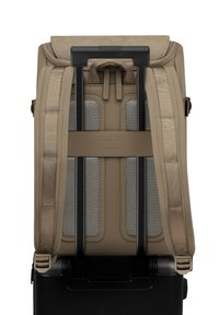 Beige reistas met gevoerde schouderbanden, grijze meshaccenten en een uitschuifbare hendel. Zichtbare zwarte basis met wielen aan de onderkant.