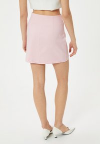 Une mini-jupe rose avec une texture lisse, dotée d'une taille ajustée et de subtiles détails de couture, associée à des chaussures à talons blanches.
