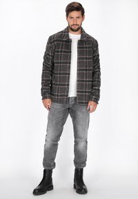 Cămașă în carouri gri cu accente negre și roșii, purtată peste o cămașă albă. Asortată cu blugi gri deschis și cizme negre cu șireturi.