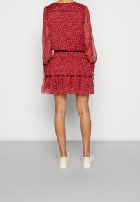 Robe rouge à imprimé floral avec de longues manches transparentes, un ourlet volanté et une taille cintrée, assortie à des baskets blanches.