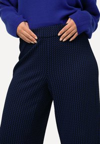 Pantalones de color azul marino con un patrón geométrico. Tienen una cintura alta y un corte relajado, combinados con un suéter azul de corte holgado.
