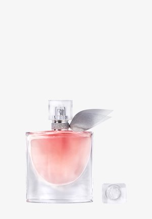 Bottiglia di profumo trasparente rettangolare con liquido rosa, nastro d'argento sul collo e tappo quadrato trasparente posto accanto su sfondo bianco.