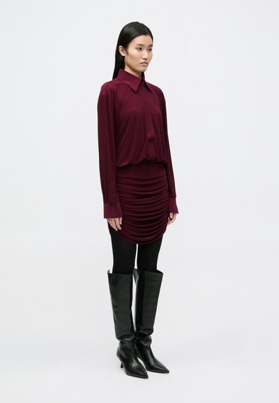 Bordo spalvos ilgomis rankovėmis palaidinė, raukšlėtas mini sijonas, juodos pėdkelnės, juodi oda kelius siekiantys batai su smailiomis noselėmis. Lygi medžiaga, prigludęs siluetas.