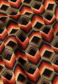 Tessuto con un motivo geometrico esagonale nei colori rosso, arancione, nero e verde, caratterizzato da un tessuto testurizzato con un design audace e vivace.