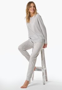 Grå långärmad topp kombinerad med ljusgrå randiga pyjamasbyxor, gjorda av mjukt tyg. Modell sitter på en vit träpall.