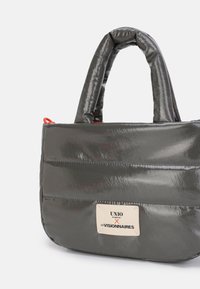 Borsa imbottita grigia con texture lucida, doppio manico corto e una vistosa targhetta con logo. Presenta un accento rosso a contrasto. Forma rettangolare.