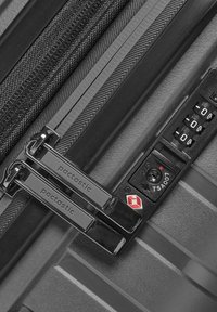 Primo piano di una valigia nera rigida che mostra zipper metallici doppi etichettati "pactastic" e un lucchetto a combinazione approvato dalla TSA.