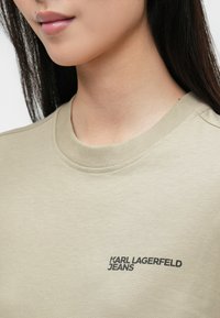 Beżowa bawełniana bluza z okrągłym dekoltem, z czarnym logo "KARL LAGERFELD JEANS" nadrukowanym po lewej stronie. Gładka struktura.