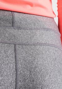 Leggings sportivi grigi con tessuto testurizzato, dotati di vita alta e cuciture visibili. Il materiale sembra elastico e resistente.