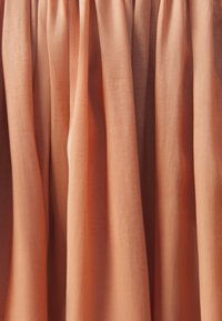 Peach-colored fabric with a smooth texture, forming pleats. The material appears lightweight and flowing, enhancing light diffusion.