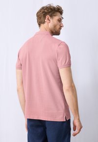 Růžová polokošile s krátkým rukávem, hladká textura, boční rozparky a klasický límec, nošená s námořnickými šortkami.