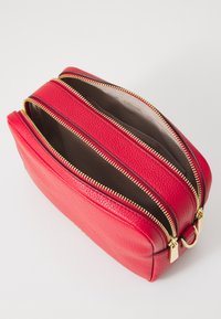 Borsetta cosmetica rossa in pelle con due cerniere dorate e una finitura testurizzata. L'interno è di un colore chiaro uniforme, spazioso e di forma rettangolare.