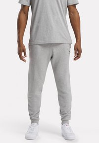 Grijze katoenen shirt met korte mouwen en bijpassende joggingbroek. De broek heeft elastische boorden en een klein zwart logo op de linker bovenbeen. Witte sneakers.