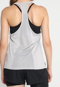 Canottiera sportiva grigia chiara con schiena in rete, design a corsetto e spalline nere a contrasto, abbinata a pantaloni corti neri.
