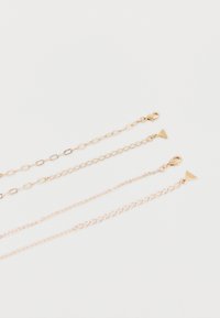 Quatre rallonges de chaîne délicates en or avec fermoirs mousquetons et extrémités en forme de triangle, disposées côte à côte sur un fond blanc.