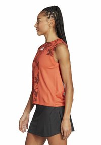Top atlético en un vibrante color naranja con un diseño texturizado, combinado con una falda negra con pliegues. Fabricado con un tejido ligero para facilitar el movimiento.