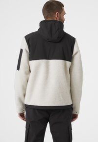 Chaqueta de forro polar con un cuerpo texturizado blanco, hombros y capucha negros, y un acento negro en la manga izquierda. Presenta un ajuste relajado y capucha.