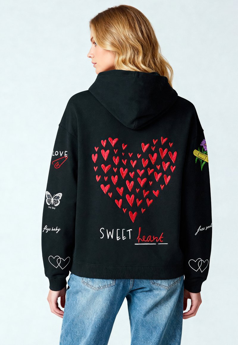Sudadera negra con patrones de corazones rojos, texto "SWEET heart", mariposas y detalles florales. Material suave con un ajuste relajado.