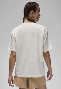 Cream-colored t-shirt with a relaxed fit, short sleeves, and a round neckline, shown from the back; worn with beige shorts.