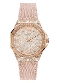 Reloj Guess con caja octagonal en oro rosa, adornos de cristal y una correa de tela de color rosa claro. Los detalles notables incluyen una correa texturizada y acentos numéricos.