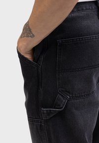 Sorte denimbukser med en sidelomme og detaljeret syning. Stoffet har en struktureret overflade og en slank, skræddersyet pasform.