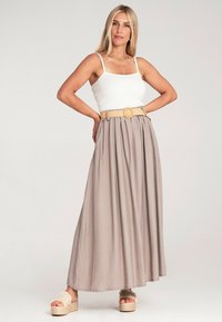 Hellbeige Maxirock mit elastischem Taillenbund, strukturiertem Stoff und einem geflochtenen Gürtel. Kombiniert mit einem enganliegenden weißen Tanktop und Plateausandalen.