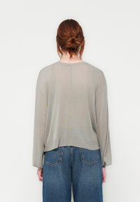 Lichtgrijze, ruime trui met lange mouwen, geribbelde zoom en een iets gekorte achterkant, gecombineerd met blauwe high-waisted jeans.