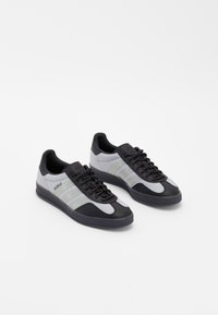 Gray and black athletic sneakers with synthetic upper, textured fabric, black laces, and three white side stripes. Rubber outsole design.