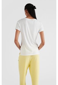 Witte katoenen t-shirt met korte mouwen, ronde hals, gladde textuur en subtiele gradient effect naar de zoom, gecombineerd met gele broek.