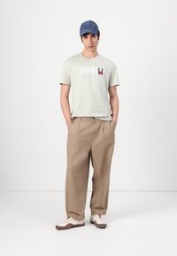 Light grey cotton T-shirt with "TOMMY" logo, beige wide trousers, and blue cap. White sneakers with brown accents.