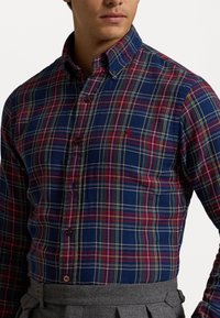 Koszula flanelowa w niebiesko-czerwono-żółtą kratkę, z kołnierzykiem na guziki i logo na lewej piersi. Teksturowany materiał.