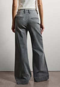 Brede, hooggewaist grijze broek gemaakt van denim, met dubbele achterzakken en een soepele textuur. Minimalistisch ontwerp met strakke lijnen.