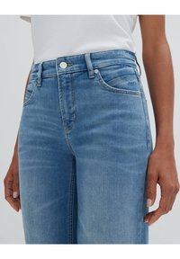 Des jeans en denim bleu clair présentent une taille mi-haute, un design à cinq poches, des boutons argentés et un léger délavage le long des jambes.