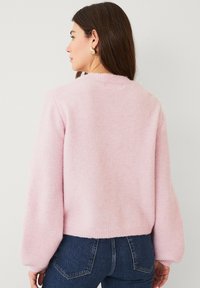 Roze, fluffy gebreide trui met een ronde halslijn en lange, afgeronde mouwen. Geribde zoom en manchetten. Achteraanzicht laat de zachte textuur en casual pasvorm zien.