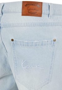 Light blue denim jeans featuring a brown leather label with embossed text and a white embroidered signature on the back pocket.