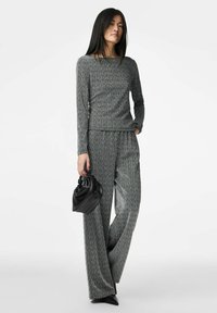 Pilkas megztas dviejų dalių komplektas, sudarytas iš ilgomis rankovėmis megztuko ir plačiomis kelnėmis, papildytas juoda rankine ir smailiais juodais batais.