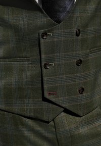 Grüner karierter Weste aus strukturiertem Stoff mit einem doppelt geknöpften Design, das dunkle Knöpfe und ein kontrastierendes rotes Steppdetail aufweist.