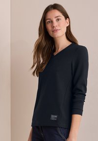 Huppari V-neck pitkällä hihalla tumman meriintsin värissä, rakenteellisessa kankaassa, pieni logo-ompeluhelma, istuvat hihat ja rento muotoilu.