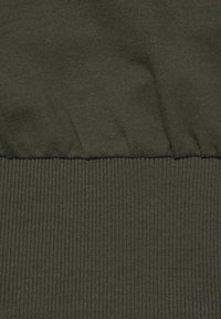 Dunkelgrüner Stoff mit einem strukturierten, gerippten Design am unteren Ende. Glatter oberer Abschnitt mit gerafftem Detail entlang der Naht.