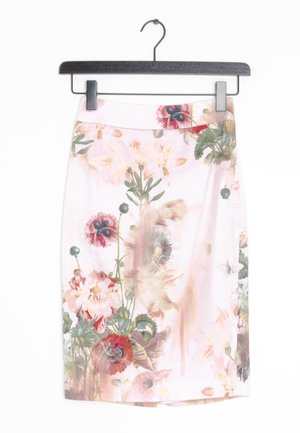 Jupe rose pâle jusqu'aux genoux avec un motif floral délicat en rouge, vert et beige suspendue à un cintre noir.