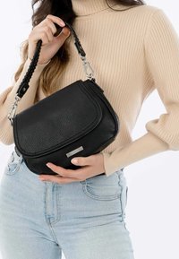 Czarna skórzana torba na ramię o fakturowanym wykończeniu i plecionym pasku. Z przodu ozdobiona srebrnym elementem metalowym. Prostokątny kształt.
