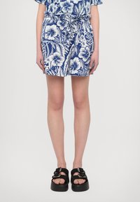 Marineblå shorts med hvitt blomstermønster, elastisk midjebånd med justerbar snøring, kombinert med svarte platåsandaler med vevde stropper.
