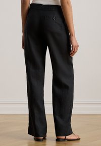 Fekete lenvászon nadrág egyenes szárú kialakítással, két hátsó zsebbel és sima textúrával. Minimalista fekete szandállal viselve.