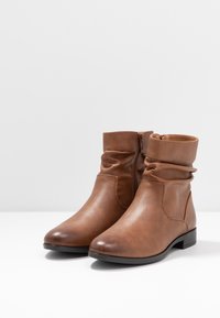 Bottines en cuir marron avec un pli décontracté à la cheville et une fermeture éclair sur le côté, présentant un bout rond et un petit talon carré.