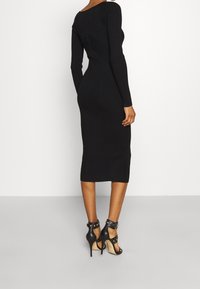 Schwarzes, geripptes Langarmkleid mit taillierter Silhouette und knielangem Saum. Getragen mit schwarzen, schmalen, hochhackigen Sandalen.