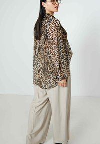 Blouse met luipaardprint en ruches aan de halslijn, van lichtgewicht stof en met lange mouwen. Gepaard met losse, lichtbeige broeken.