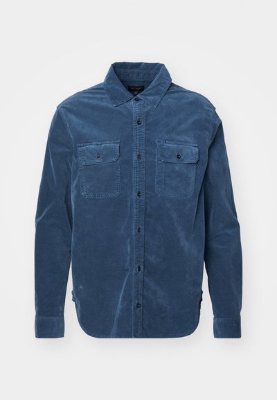 Camisa de pana azul de manga larga con dos bolsillos en el pecho, cierre de botones y puños ajustables, que presenta una textura suave y un cuello clásico.