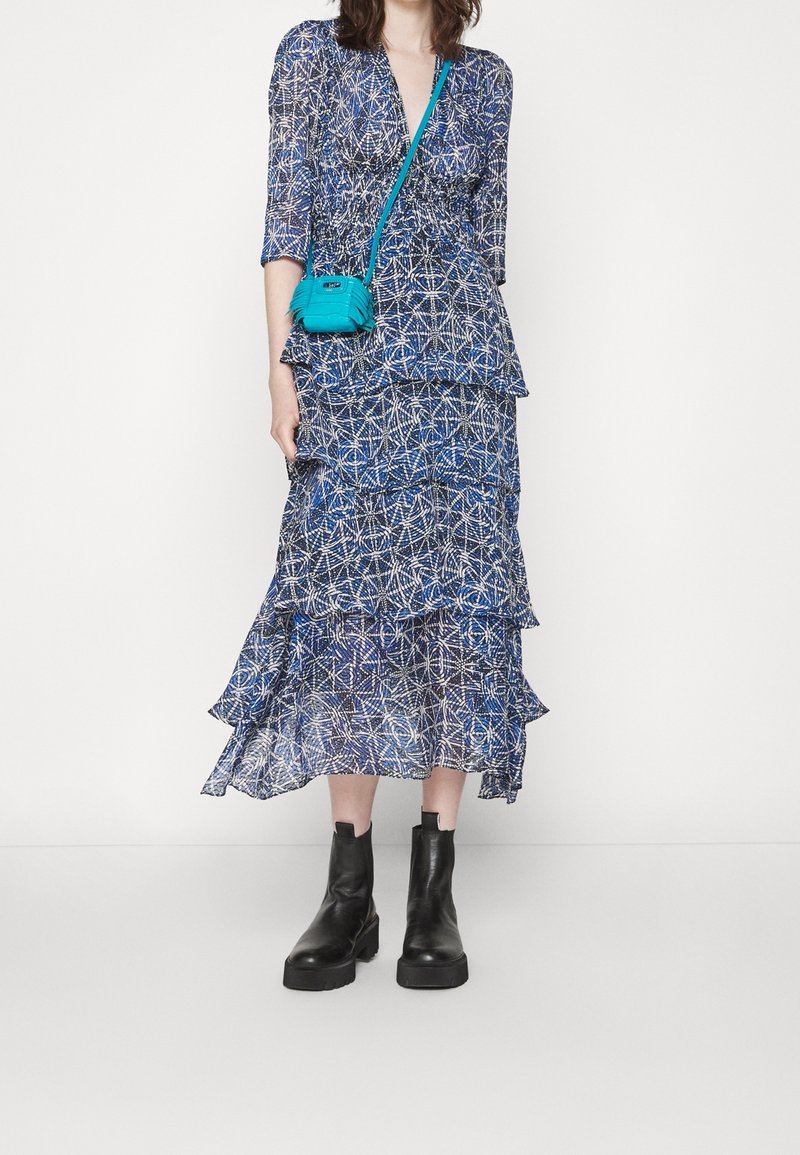 Vestido azul con estampado y volantes en capas, combinado con un pequeño bolso cruzado turquesa y botas de tobillo negras y gruesas.