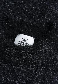 Czarna, puszysta tkanina z srebrnymi włóknami, z białą etykietą częściowo widoczną z czarnym wzorem logo. Miękka tekstura i puszysty wygląd.