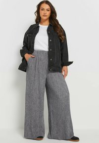 Svart denimjacka över en vit t-shirt, med breda, grå ribbade byxor med en texturerad yta och en avslappnad passform.